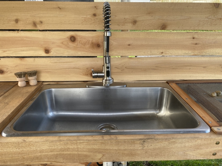 Stainless steel sink with a modern faucet in a wooden outdoor kitchen