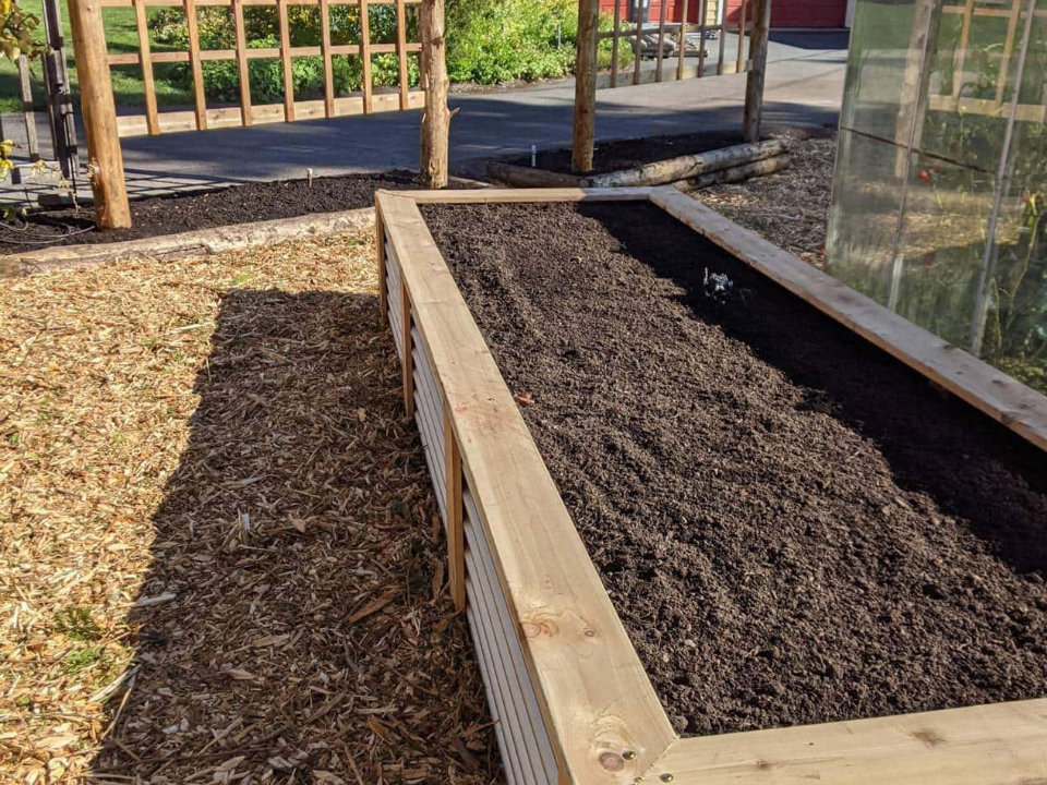 New wooden raised garden bed filled with dark soil, ready for planting.